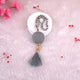 Decorative necklace with a gray pendant and tassel on a pink textured background with flowers.