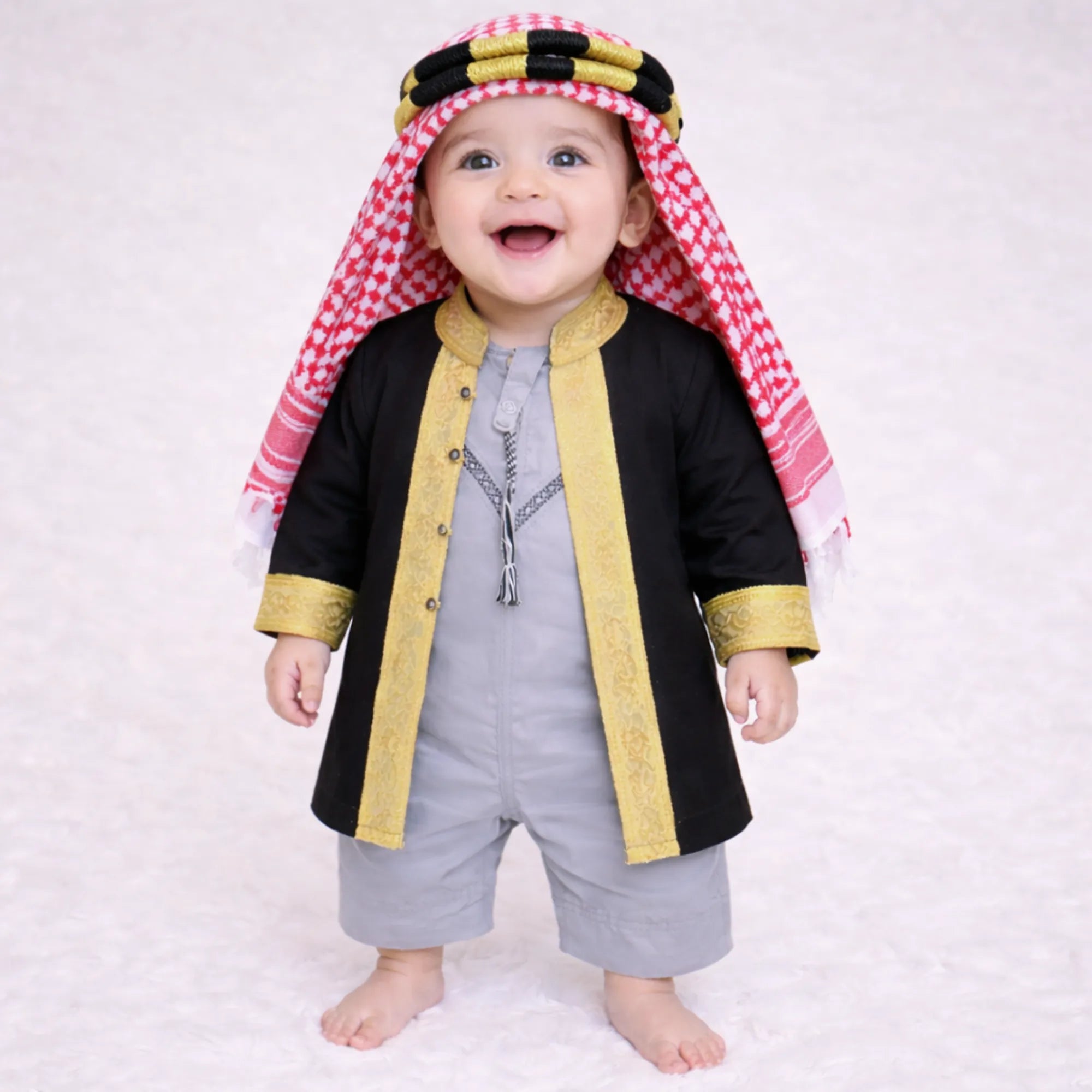Baby boy wearing traditional black and gold embroidered thobe with red and white checkered headscarf Main image