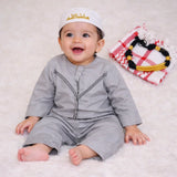 Baby boy in traditional grey thobe with Islamic cap, sitting on soft white surface