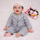 Baby boy in traditional grey thobe with Islamic cap, sitting on soft white surface