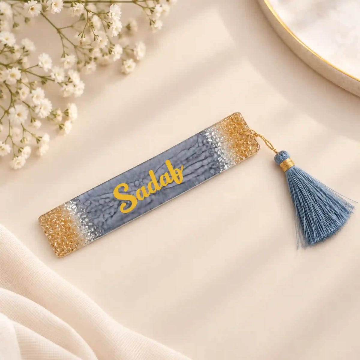 Decorative bookmark with tassel on a fluffy white surface with pink flowers.