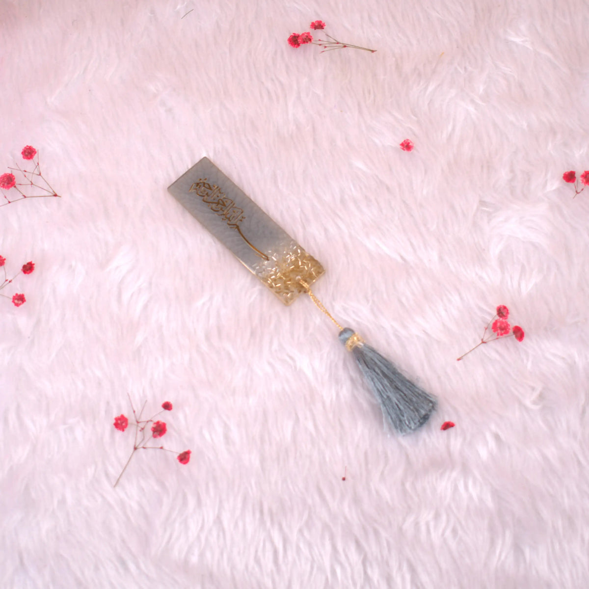 Decorative bookmark with tassel on a soft pink background with small red flowers.