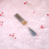 Decorative bookmark with tassel on a soft pink background with small red flowers.