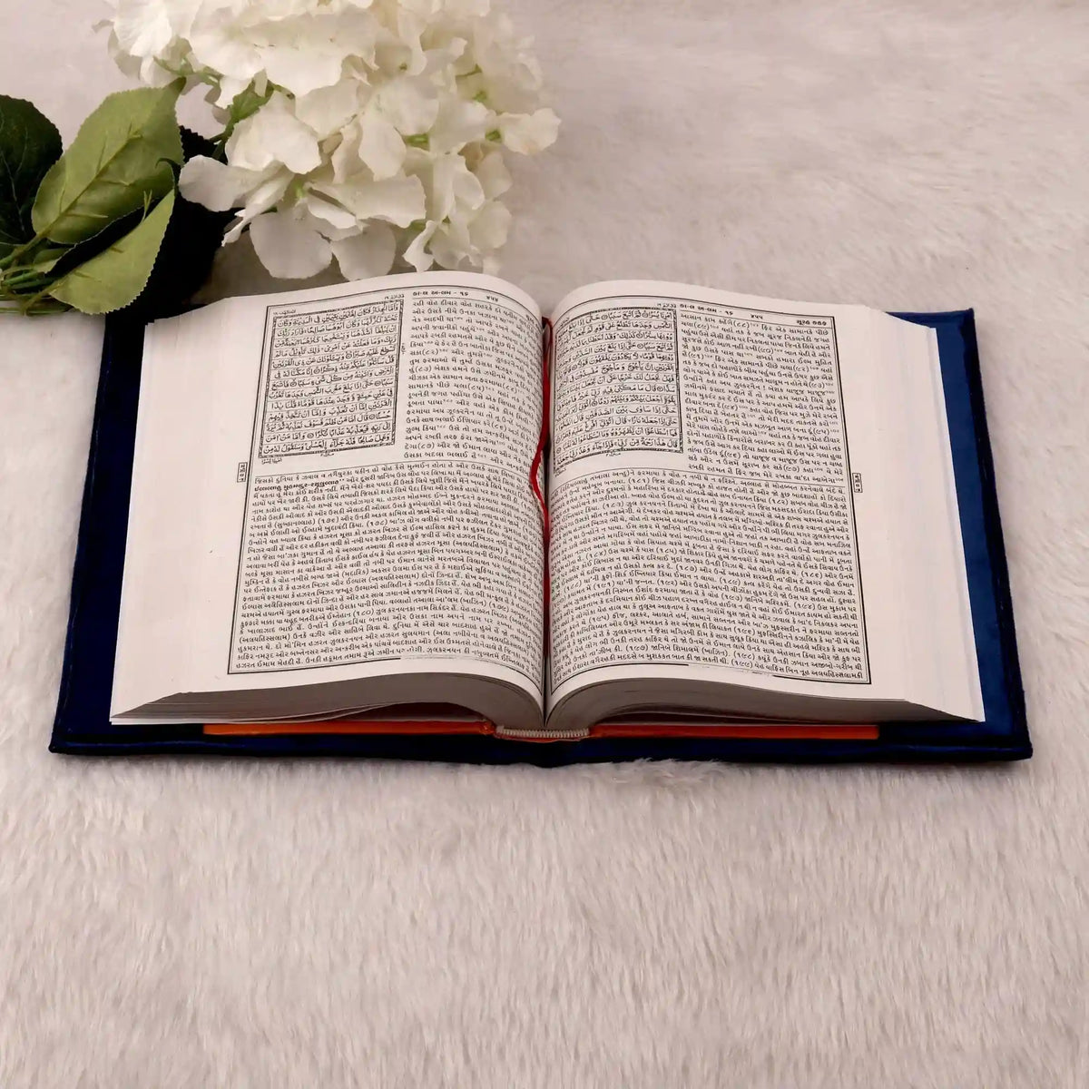Open book on a light surface with white flowers and green leaves.