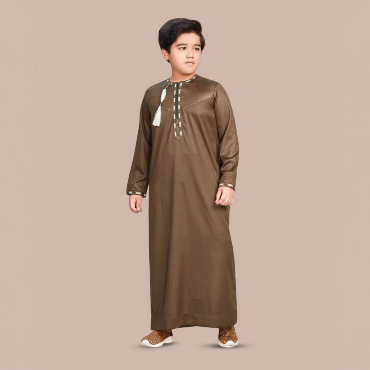 Omani Style Brown Kids Thobes in full-length design with white tassel, perfect for festive occasions. Elegant traditional wear for young boys.