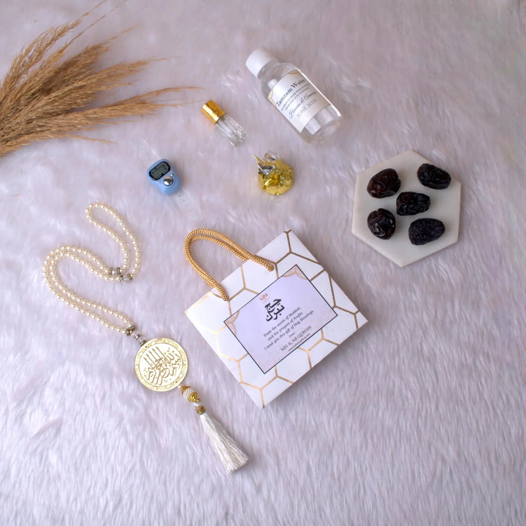 Barakah Hajj Gift Hamper Pack with tasbih, Zamzam water, Ajwa dates, and Islamic accessories on white fur background. Ideal Hajj return gift set. Main image