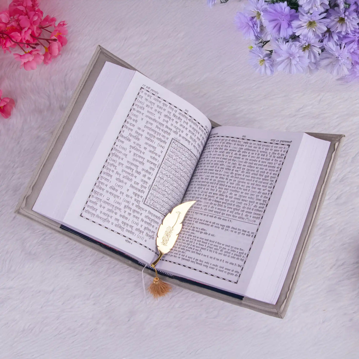 Open book with a gold leaf bookmark on a light surface with flowers around