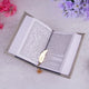 Open book with a gold leaf bookmark on a light surface with flowers around