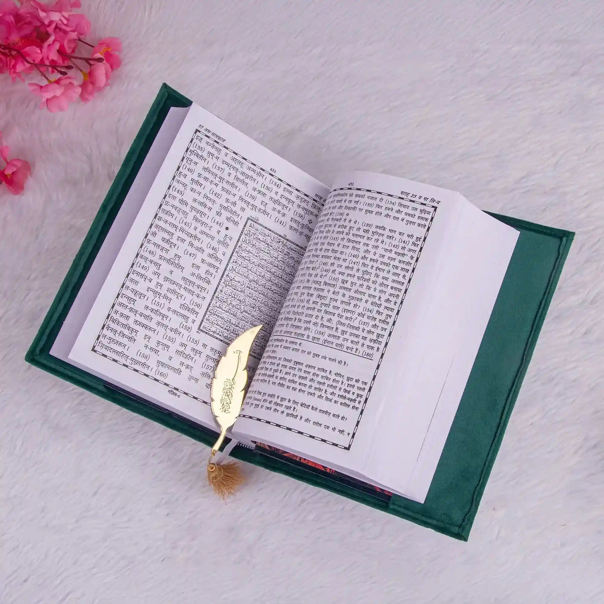 Open book with a gold leaf bookmark on a light gray surface with pink flowers.
