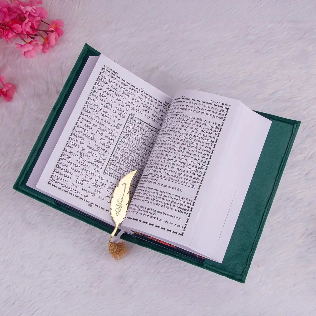 Open book with a gold leaf bookmark on a light gray surface with pink flowers.