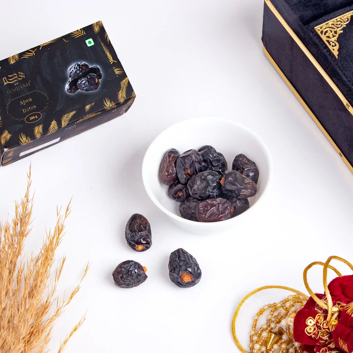Date fruits in a bowl with decorative boxes and wheat on a white background