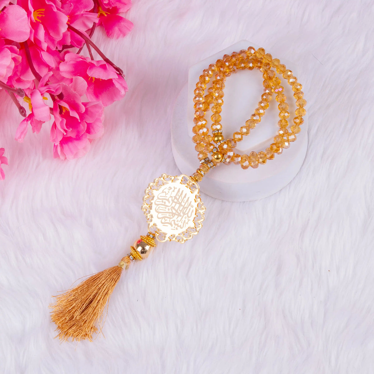 Close-up of golden crystal tasbeeh with engraved charm and tassel from the Golden Floral Pearl Rehal Hamper. Elegant Islamic prayer bead gift.
