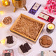 Empty wooden tray with shredded filler surrounded by Noor Al-Sweets hamper items like chocolates, cookies, almonds, and candle for Ramadan.