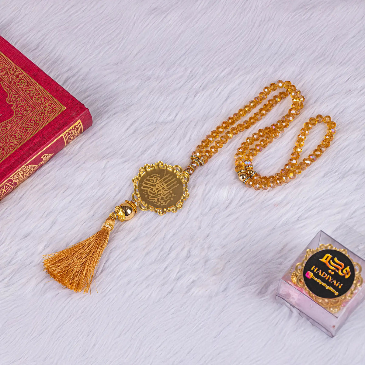 Golden Crystal Tasbeeh with 100 beads and Bismillah charm placed beside Quran, perfect for Hajj, Umrah, or Eid gifts.