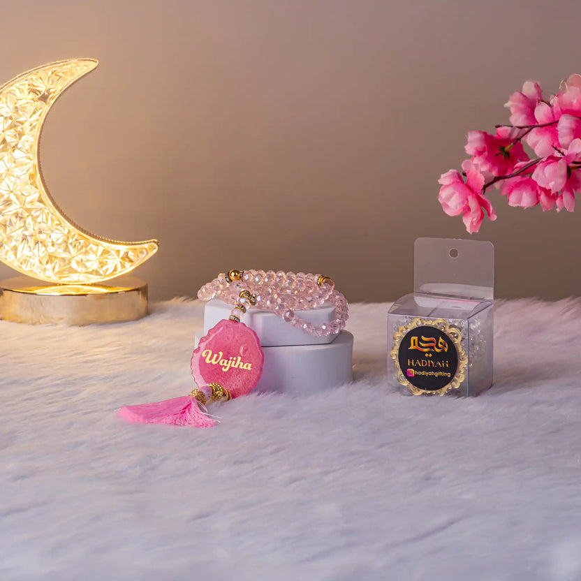 Personalized Pink Crystal Tasbeeh with name 'Wajiha' and tassel, shown with crescent lamp and gift box, perfect Hajj & Umrah gift. Main image