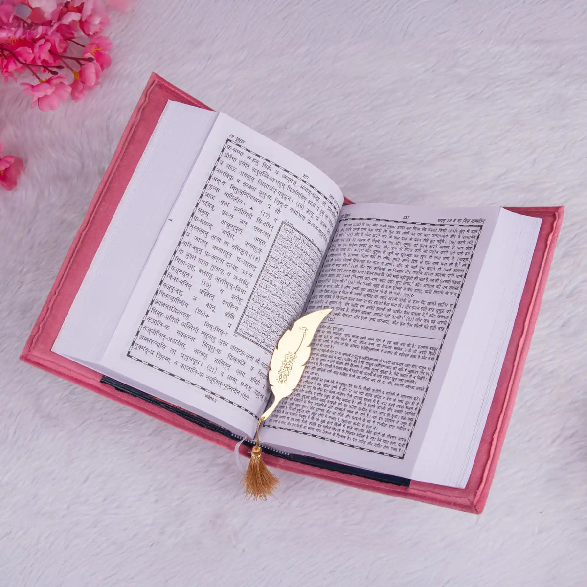 Open book with a gold feather bookmark on a light pink surface with pink flowers.