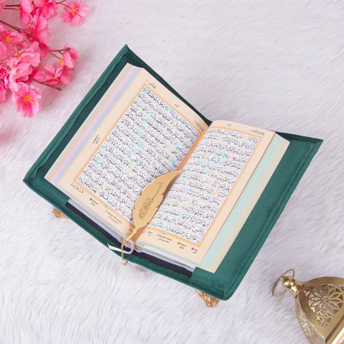 Multicolor Quran page with translation and gold feather bookmark from Green Salah Combo Hamper, styled with lantern and flowers.