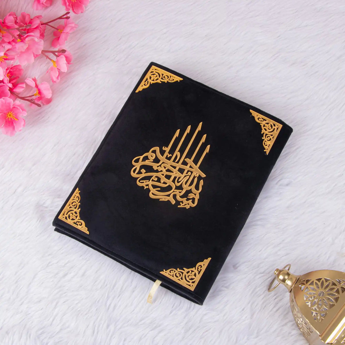 Black Kaaba Quran laid flat on white fur surface, featuring gold Arabic calligraphy, ideal for prayer and gifting.