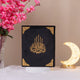 Black velvet Kaaba Quran with gold detailing, displayed upright with floral decor, a refined religious gift for special occasions.