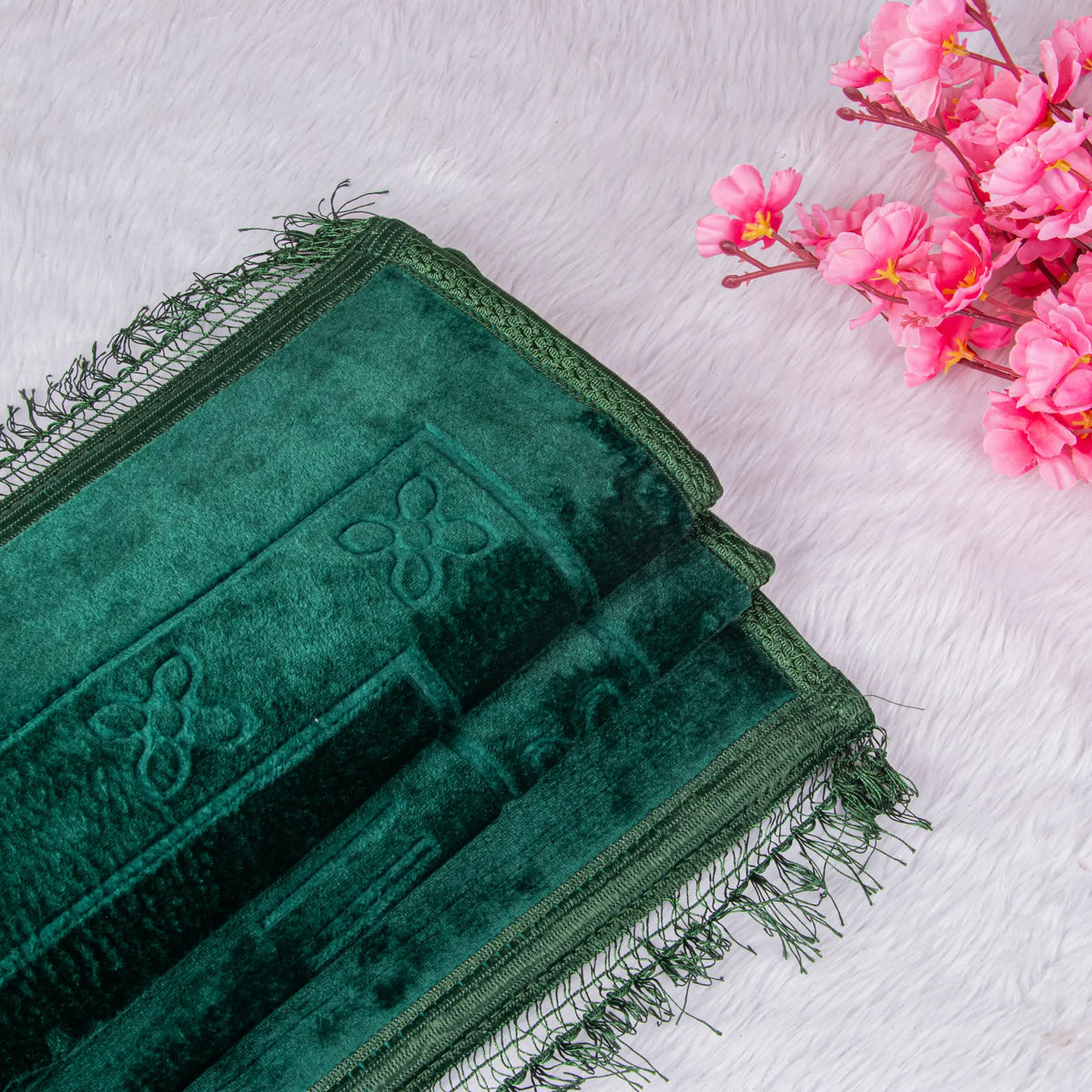 Folded dark green prayer mat with embossed design placed beside pink flowers. Part of Green Butterfly Sawab-e-Jariya Gift Set.
