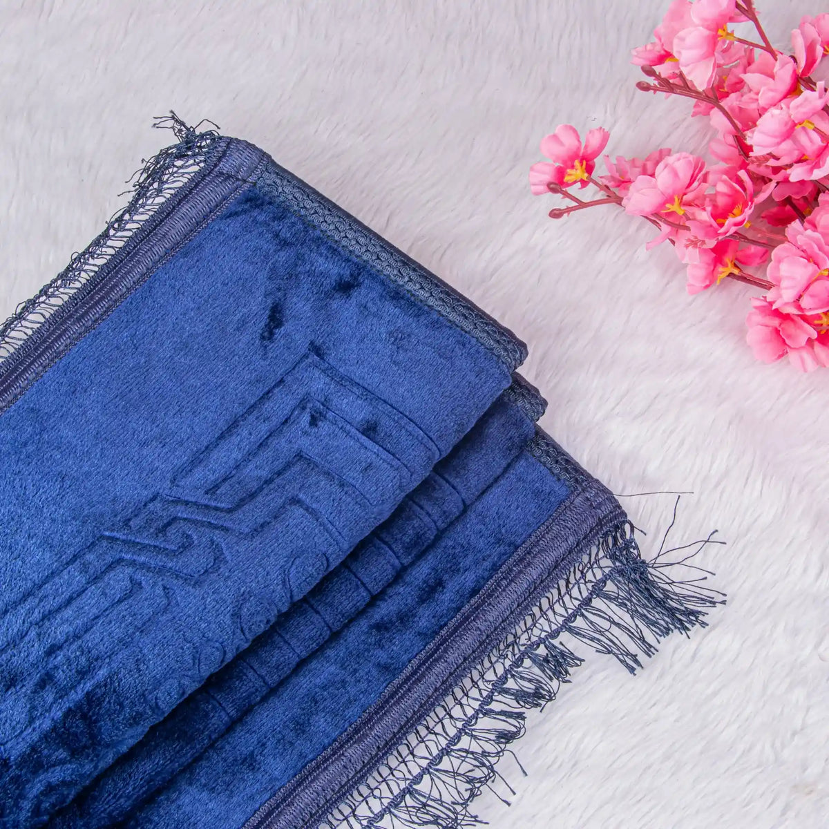 Blue towel with fringes on a light wooden surface with pink flowers.