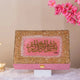 Decorative box with gold and pink design on a white surface with pink flowers in the background