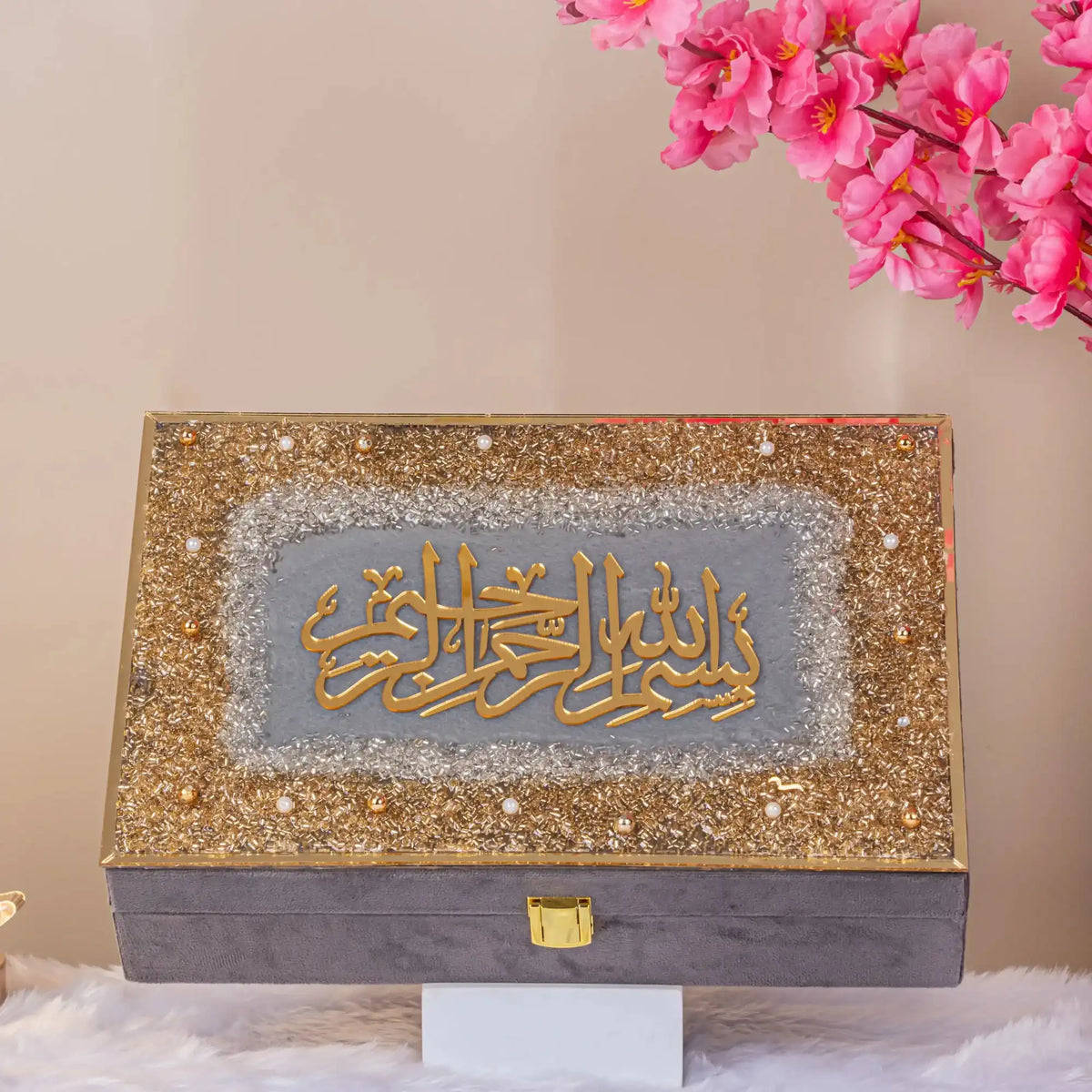 Decorative box with gold and gray design on a stand with pink flowers in the background