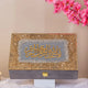 Decorative box with gold and gray design on a stand with pink flowers in the background