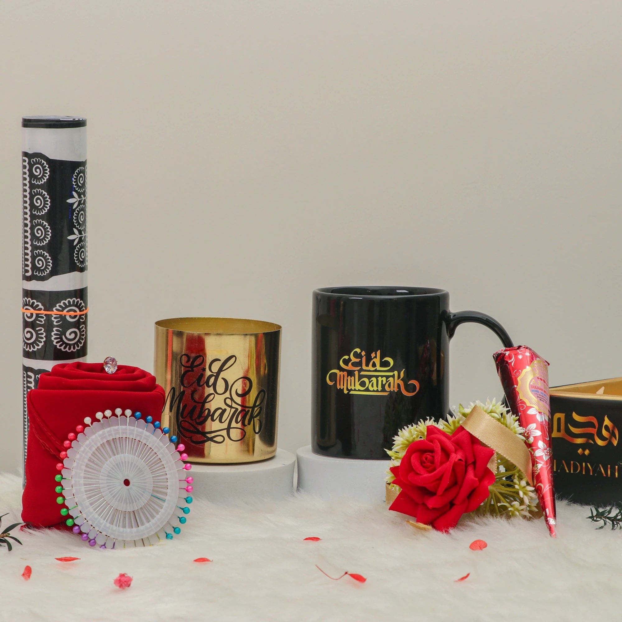 Afiyah Eid Hamper - Eid Gift Hamper for Women shown with black mug, gold candle holder, red hijab, rose, and henna cone for festive gifting.