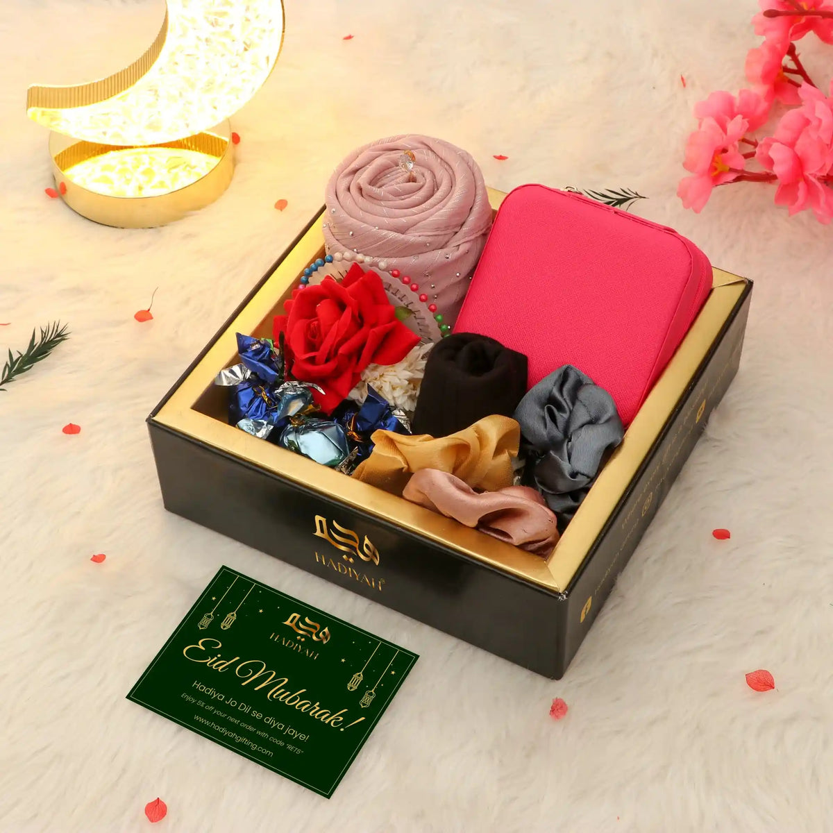 Gift set with scarves, flowers, and a card in a decorative box on a soft surface.