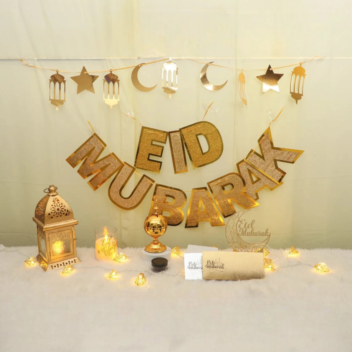 Royal Eid Glow Decor Set featuring gold 'Eid Mubarak' banner, lantern, moon and star garlands, lights, and Eidi envelopes for festive home decor.