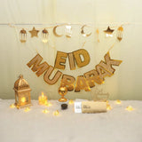 Royal Eid Glow Decor Set featuring gold 'Eid Mubarak' banner, lantern, moon and star garlands, lights, and Eidi envelopes for festive home decor.