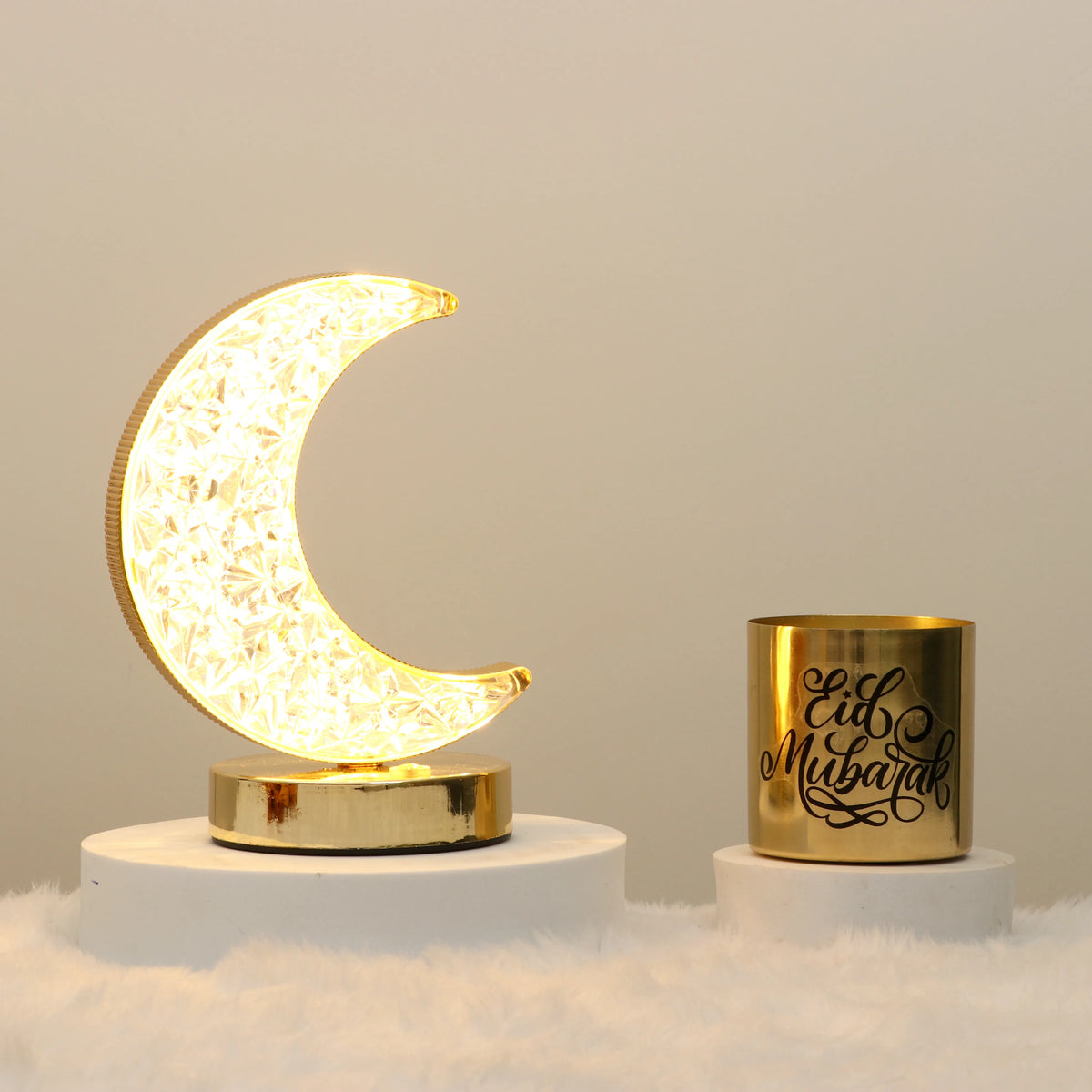 Crescent Glow Decor Set - Eid Decor featuring a glowing moon lamp with intricate patterns and a gold 'Eid Mubarak' candle on a white fur surface.