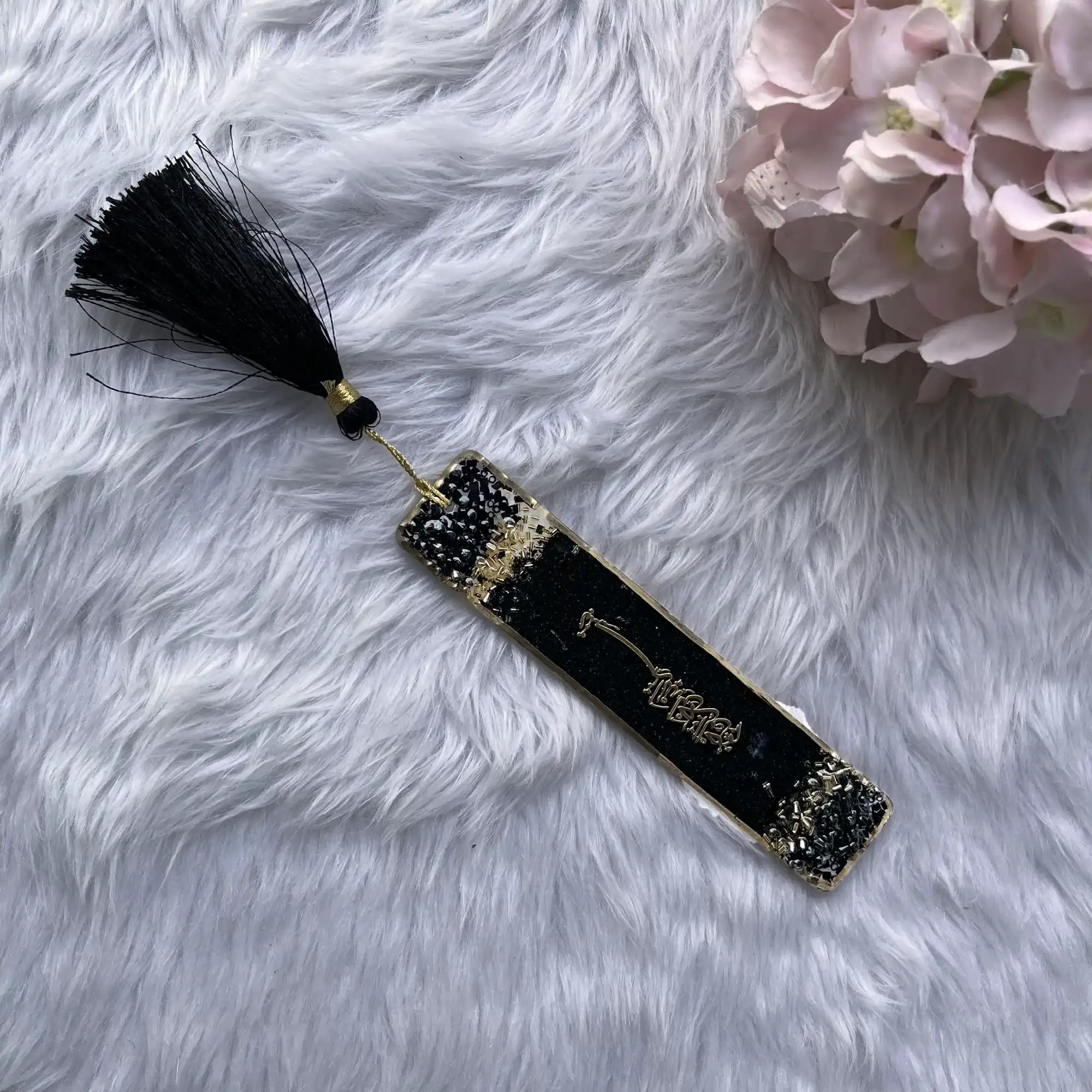 Decorative black bookmark with tassel on a fluffy white surface with pink flowers. Main image