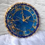 Decorative clock with blue face and gold Roman numerals on a textured white background