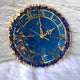 Decorative clock with blue face and gold Roman numerals on a textured white background
