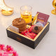 Gift box with a rosary, candle, and snacks on a white surface with decorative elements.