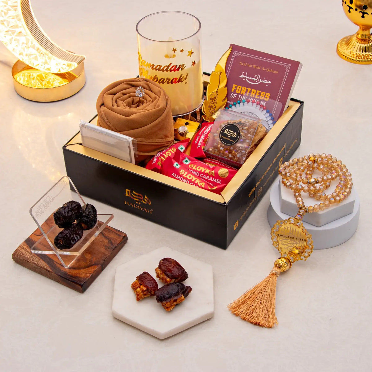 Gift box with snacks, dates, and a rosary on a decorative surface.