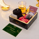 Gift box with Ramadan-themed items including a candle, card, and snacks on a white surface.