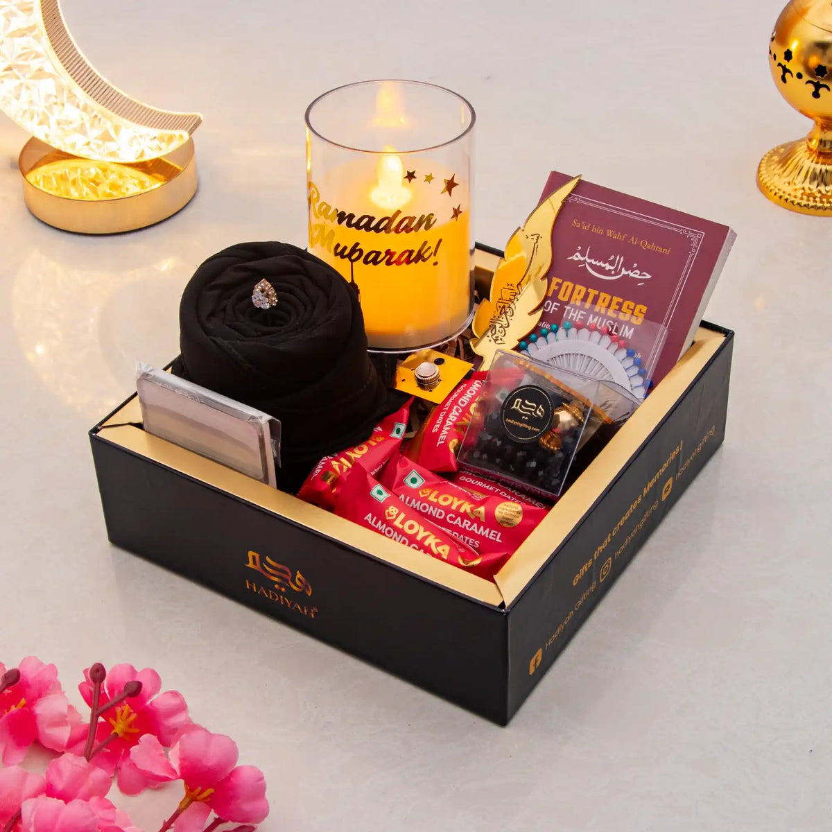 Gift box with snacks, a candle, and decorative items on a table with flowers.