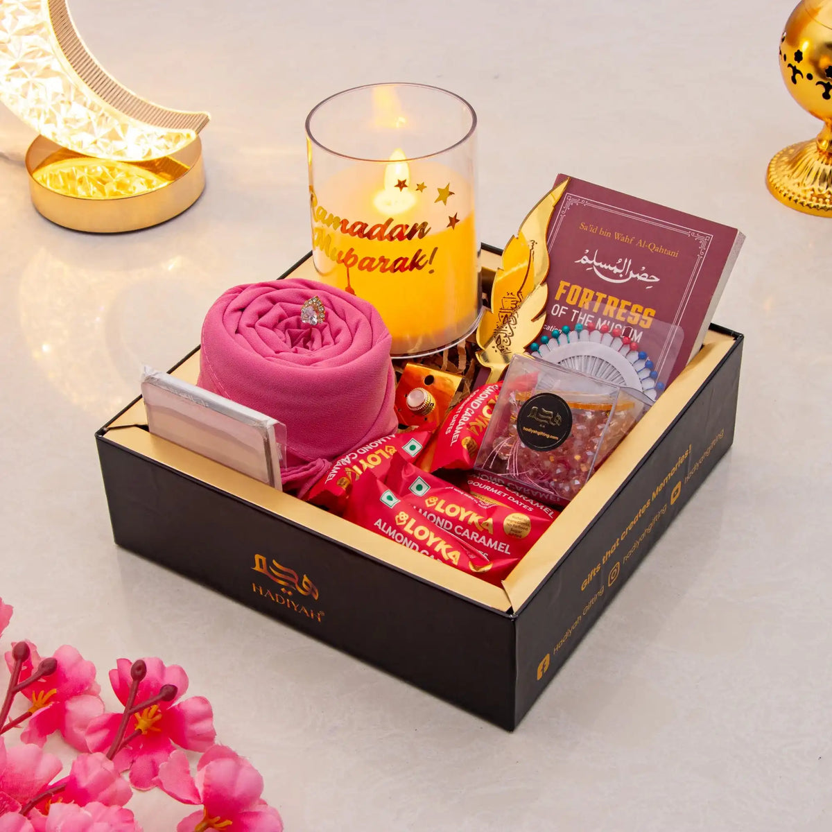 Gift box with snacks, a candle, and a card on a decorative surface.