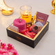 Gift box with snacks, a candle, and a card on a decorative surface.