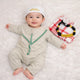 Baby boy in traditional white attire with green embroidery, lying on white fluffy surface