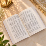 Open book with Arabic text on a light surface, with another book in the background.