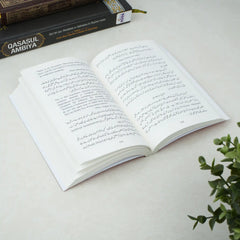 Open book with Arabic text on a light surface, with another book in the background.
