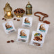 A collection of four small acrylic date stands arranged on a light-colored surface with scattered loose dates. Three of the stands feature a crescent moon and mosque design with "Ramadan Mubarak" text, while the fourth shows a printed design of a date bowl and lantern. The background includes two decorative Ramadan lanterns, a golden bowl of dates, and wooden prayer beads.