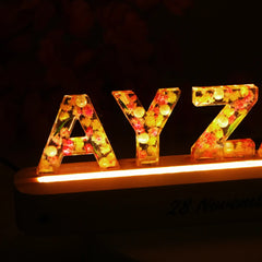 Close-up of floral resin letters 'AYZAL' with embedded LED lights on a wooden base, showcasing intricate detail and personalized decor appeal.