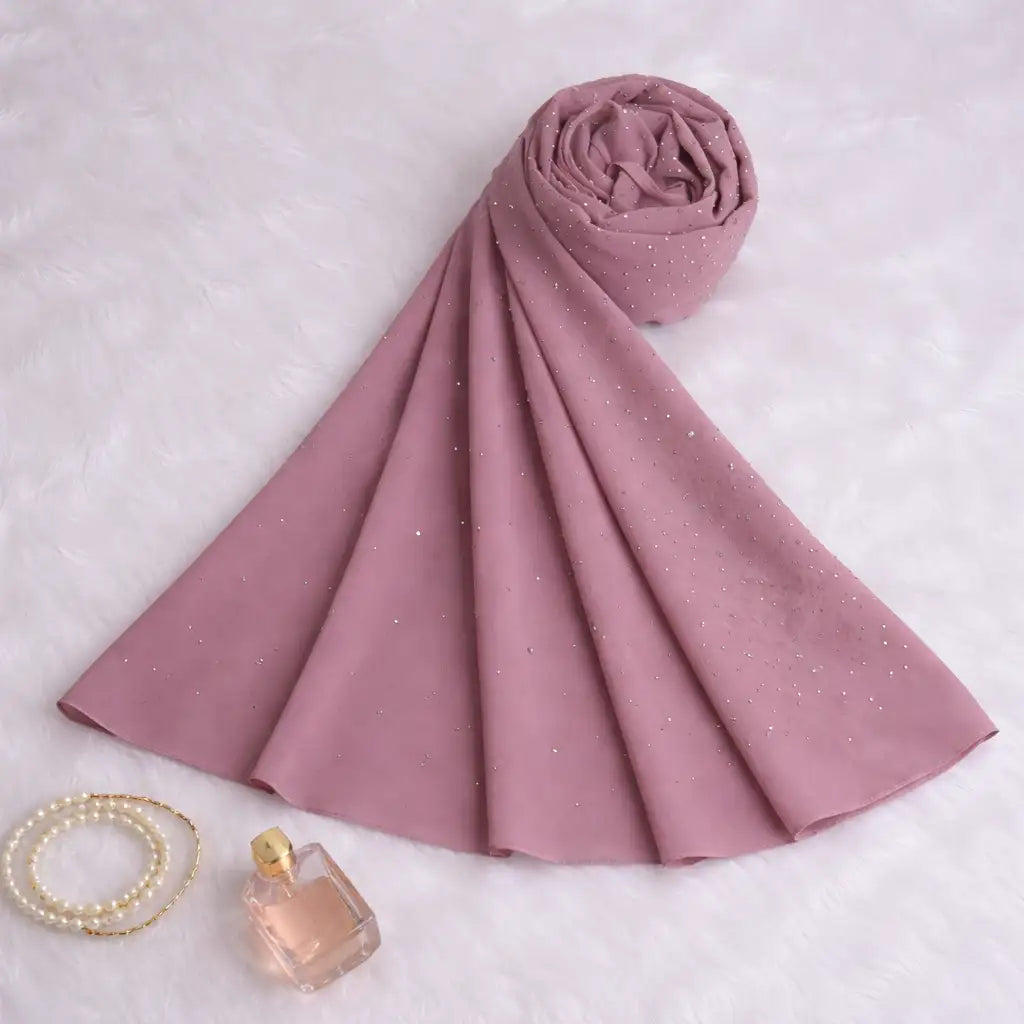 Rolled Light Pink Studded Hijab laid flat with pearl bracelet and perfume, highlighting chiffon texture and subtle sparkle for modest fashion.