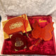 Decorative items including a butterfly ornament and religious text book on a red surface with 'Sana' branding.