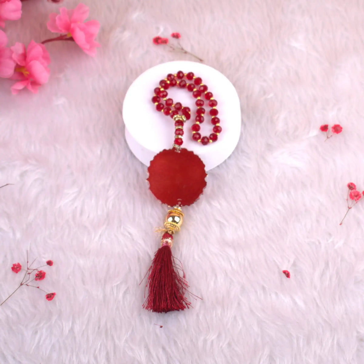 Decorative red tassel with beads on a white plate against a pink floral background